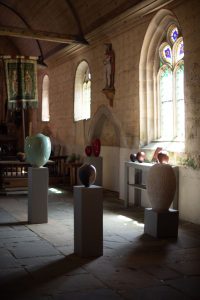 Exposition de bvases en céramique luxe par céramiste Karen Swami, 1 grand vase en céramique verte posé sur un support rectangulaire, 1 petit vase marron en poterie avec une texture glossy posé sur un support cubique, 1 grand vase de luxe en céramique d'art de couleur pastel avec une surface texturée