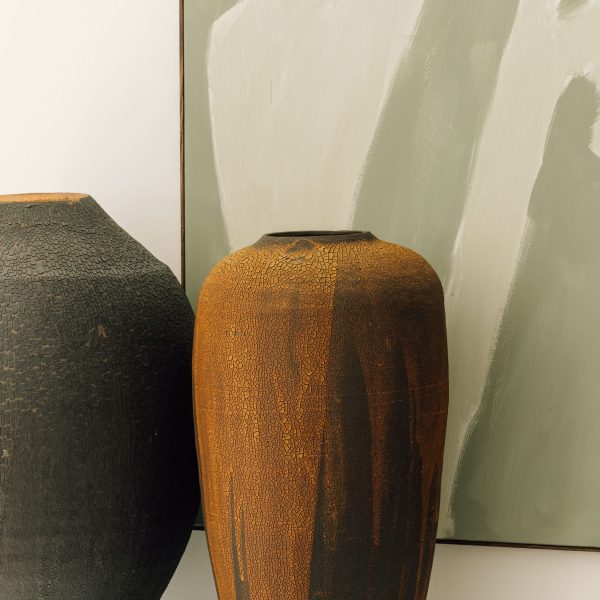 Big grey pottery vase and tall brown elongated ceramic vase with cracked textures in front of a minimalist light green acrylic painting