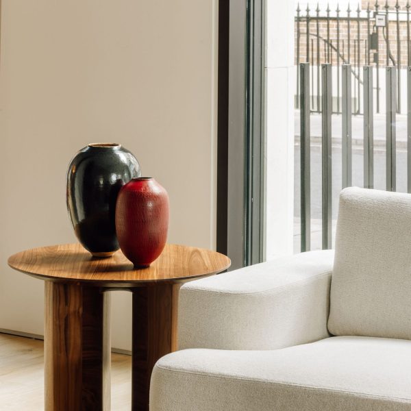 One big glossy black pottery vase and one small red textured ceramic vase, on a minimalist wooden table in a showroom